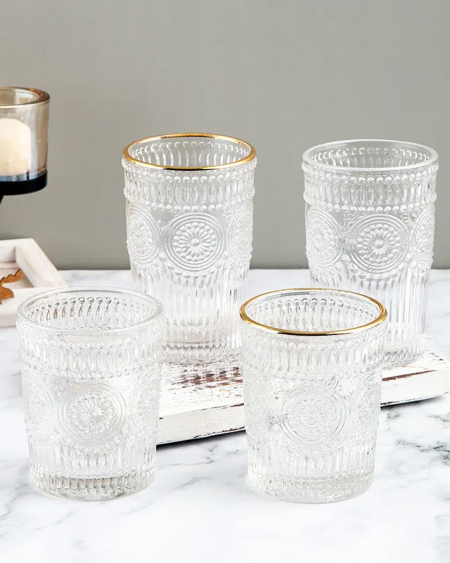 Set of clear glass tumblers with gold rims on a marble surface.