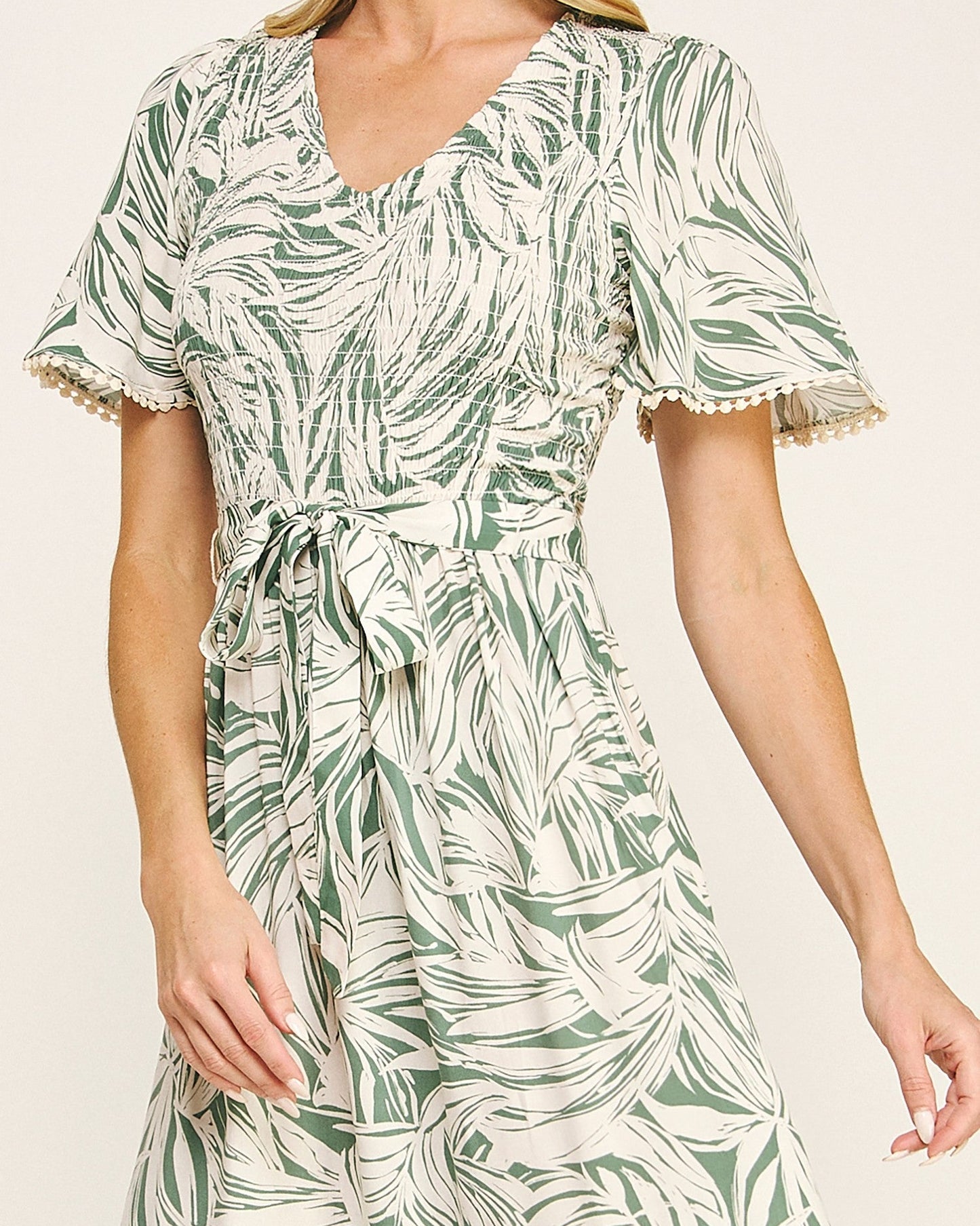 Woman wearing a green and white leaf-patterned dress on a plain background