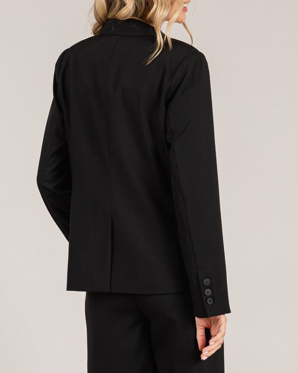 Woman wearing a black suit jacket with buttons on a plain background