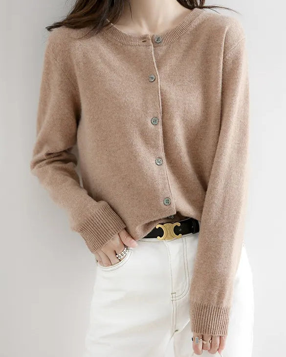 Person wearing a beige cardigan over a white outfit with a plain background