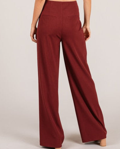 Woman wearing a white top and red high-waisted pants on a plain background