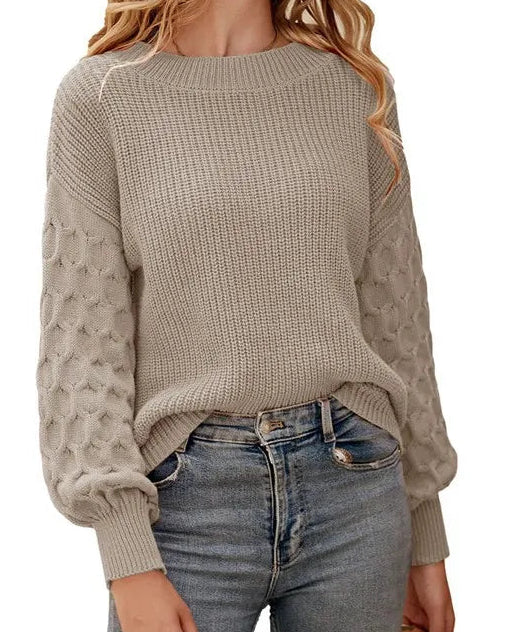 A woman wearing a beige textured knit sweater with balloon sleeves and blue jeans, shown from the neck down against a plain white background.