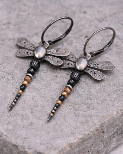 Dragonfly-shaped earrings with beaded details on a stone surface