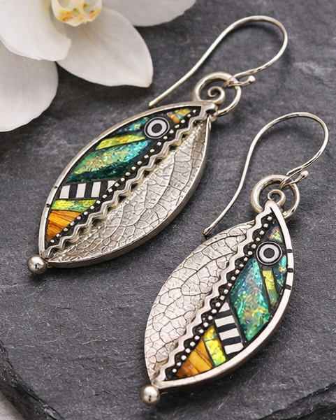 Pair of leaf-shaped earrings with colorful patterns on a dark surface.