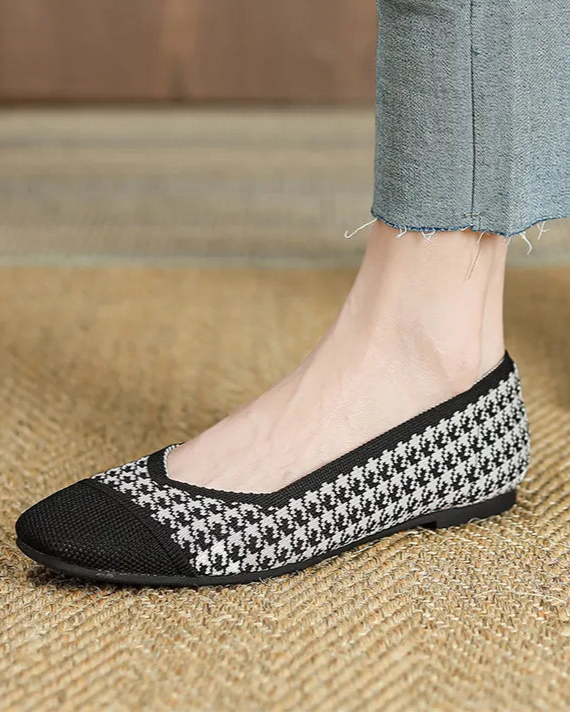 Person wearing black and white checkered shoes with blue jeans on a wooden floor.