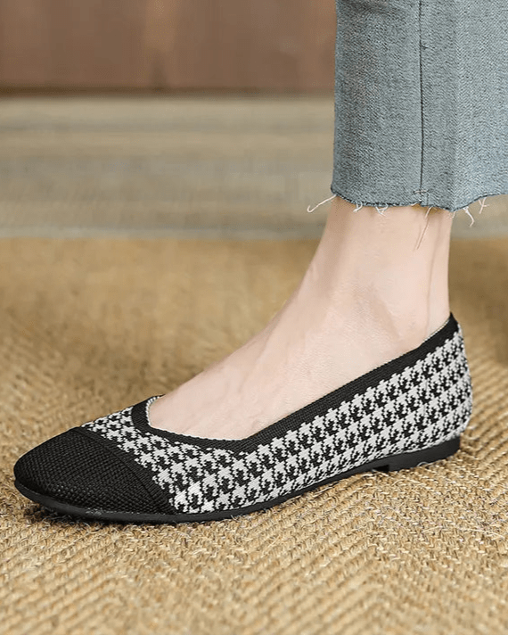 Person wearing black and white checkered shoes with blue jeans on a wooden floor.