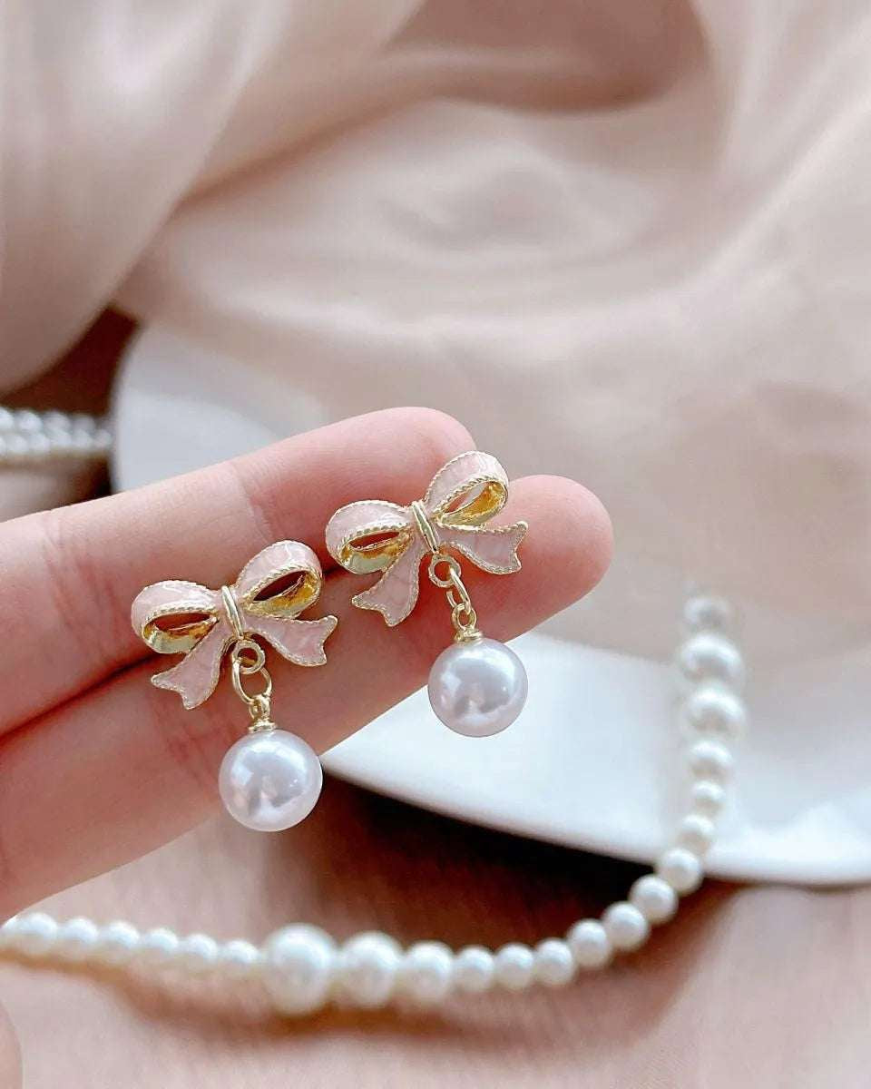 Bow and pearl earrings with gold finish displayed on jewelry card