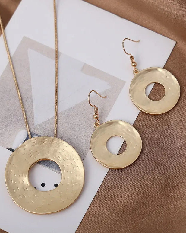 Gold necklace and earrings on a brown surface with a magazine underneath