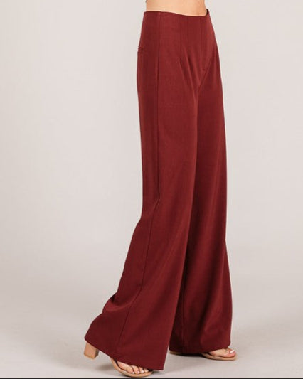Woman wearing a white top and burgundy wide-leg pants on a plain background