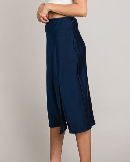 Woman wearing navy blue wide-leg pants and a white top on a plain background