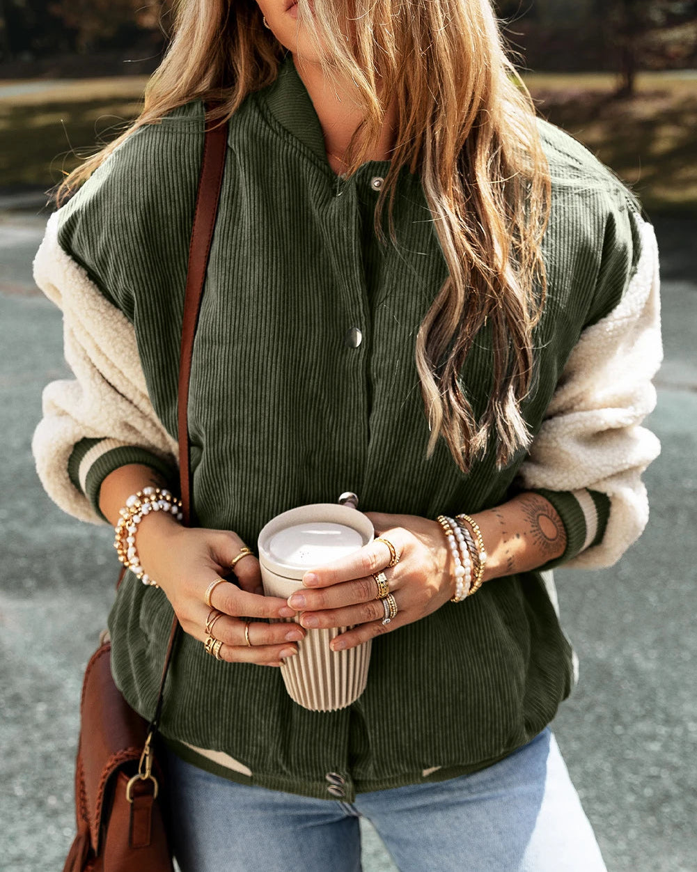 Person wearing a green jacket with white sleeves, holding a cup outdoors.