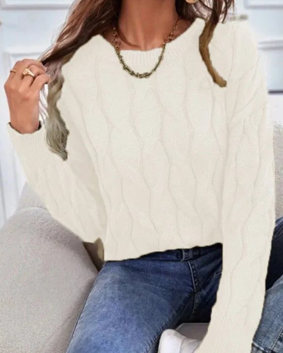 Person wearing a cream cable knit sweater and blue jeans sitting on a couch.