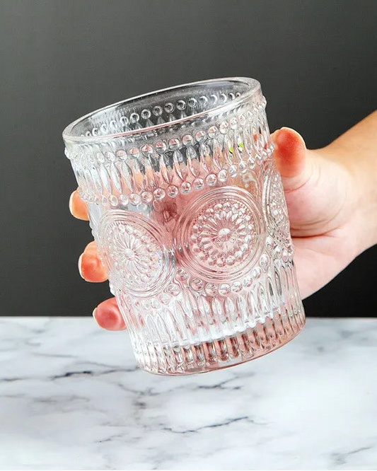 Hand holding a decorative glass tumbler on a marble surface with a dark background