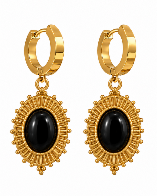 Gold huggie hoop earrings with oval black onyx centers, shown on a white background and worn on a model's ear.