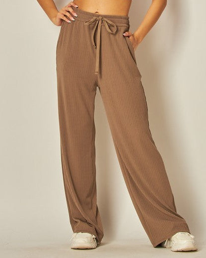 Woman wearing a white crop top and brown high-waisted pants against a plain background