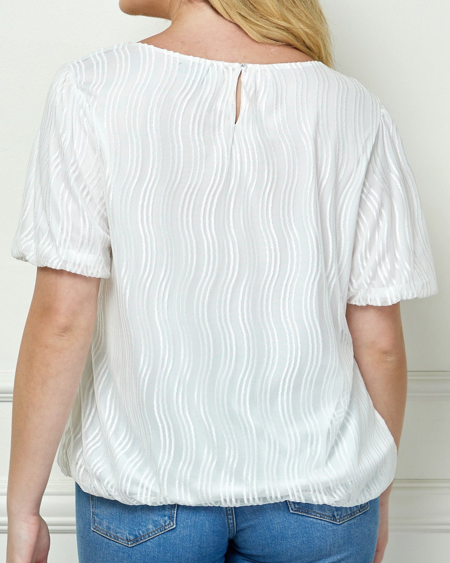 Woman wearing a white blouse with ruffled sleeves against a white wall.