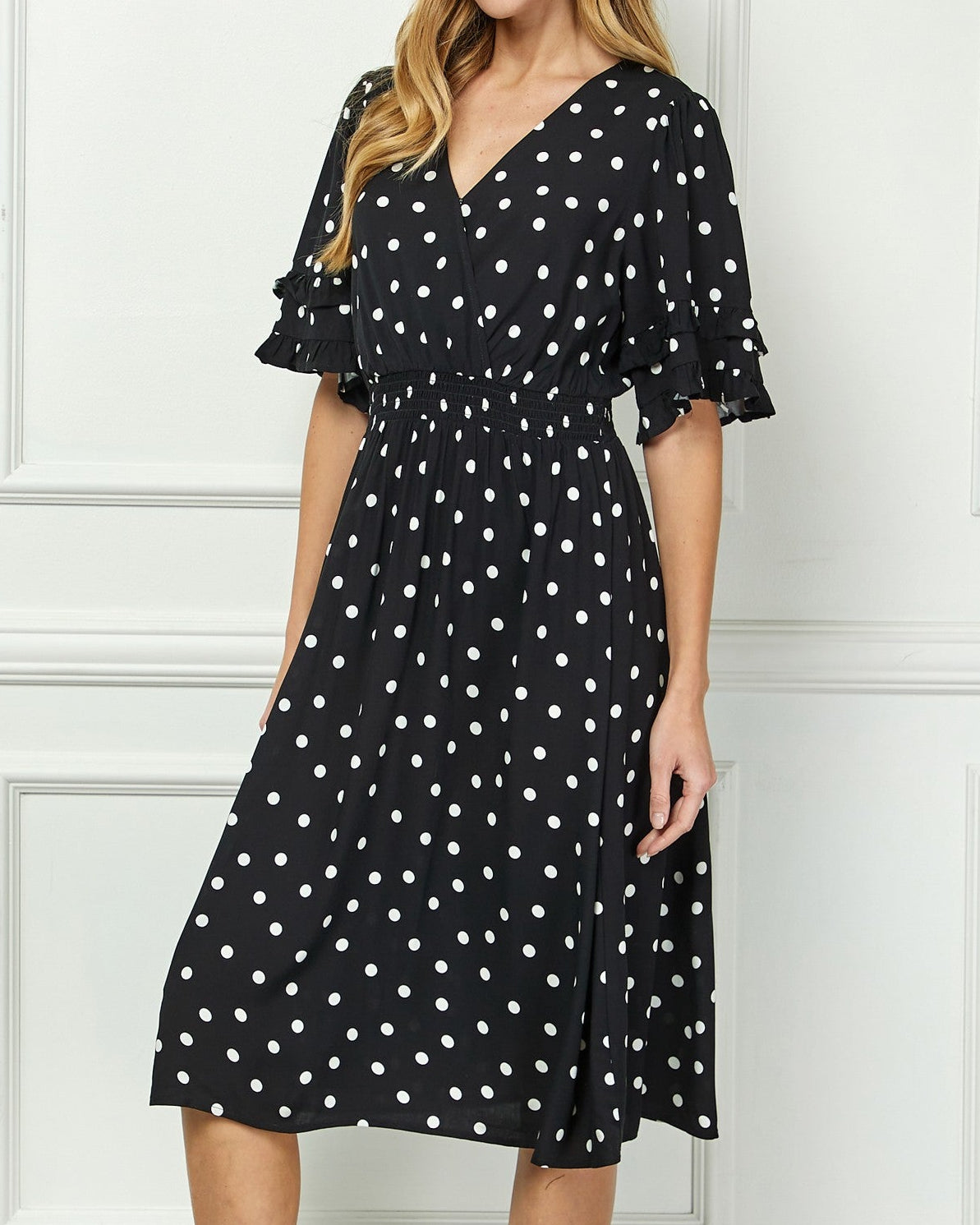 Woman wearing a black dress with white polka dots against a white wall.