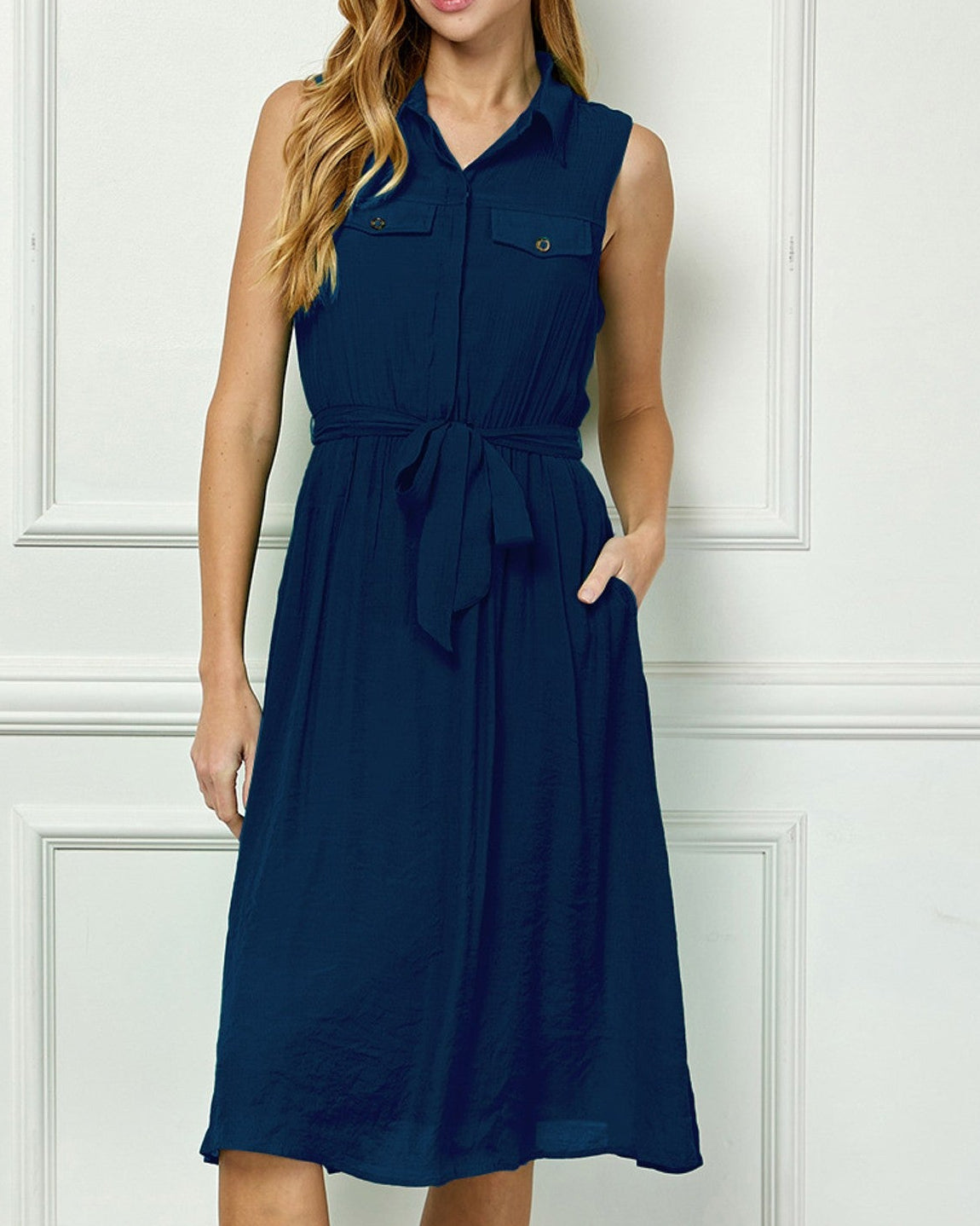 Woman wearing a navy blue dress against a white paneled wall.