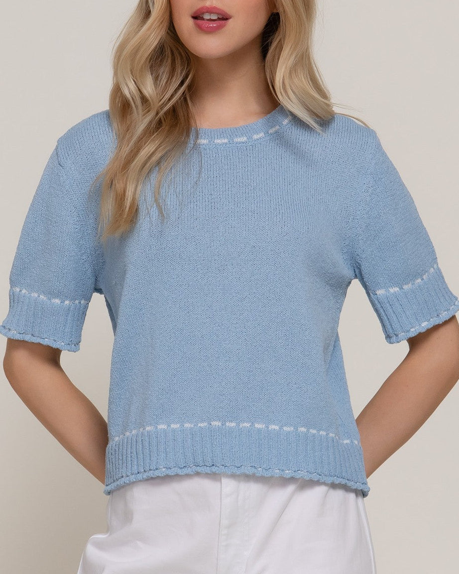 Woman wearing a light blue knit top with white trim against a plain background