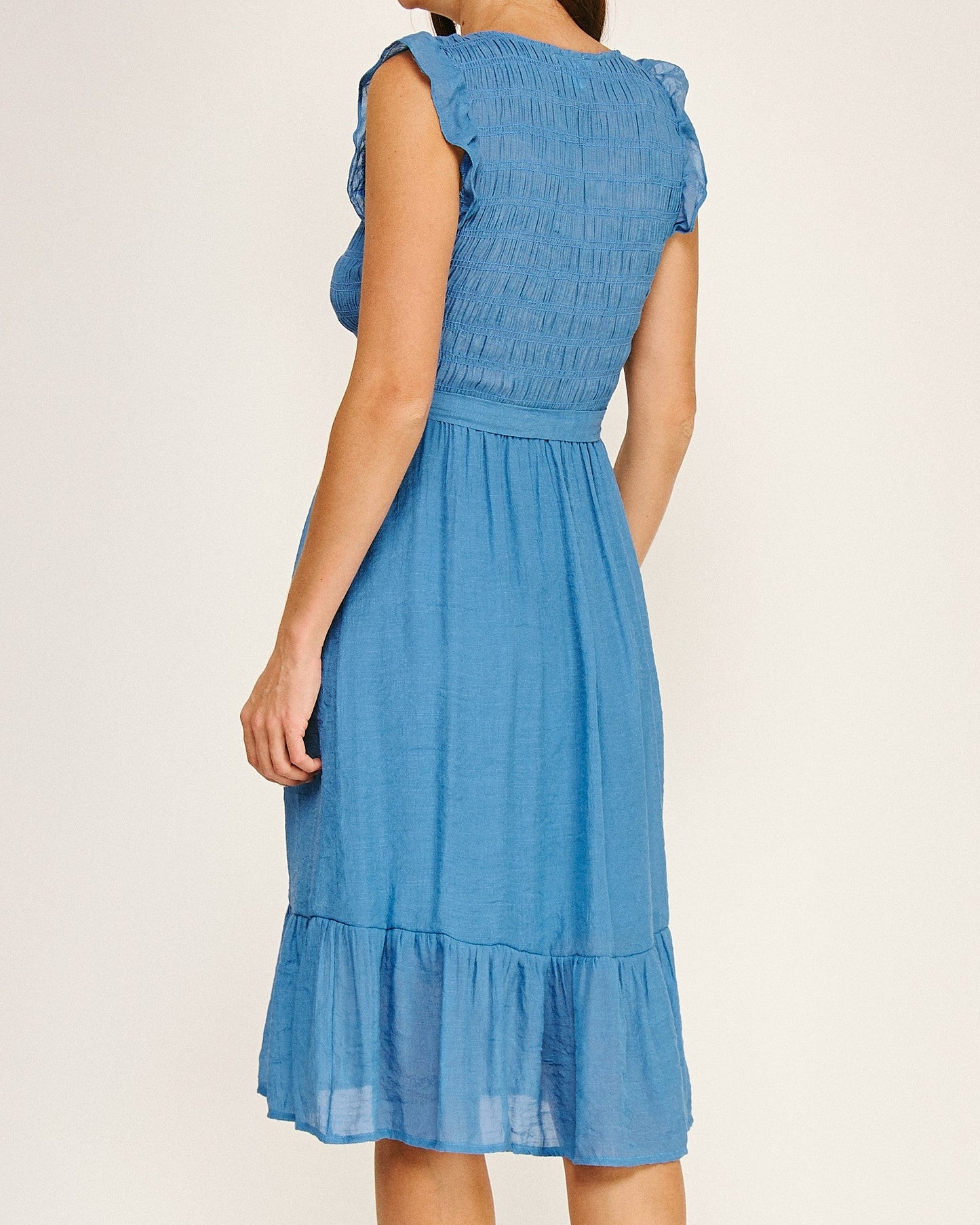 Woman wearing a blue dress with ruffled sleeves on a plain background