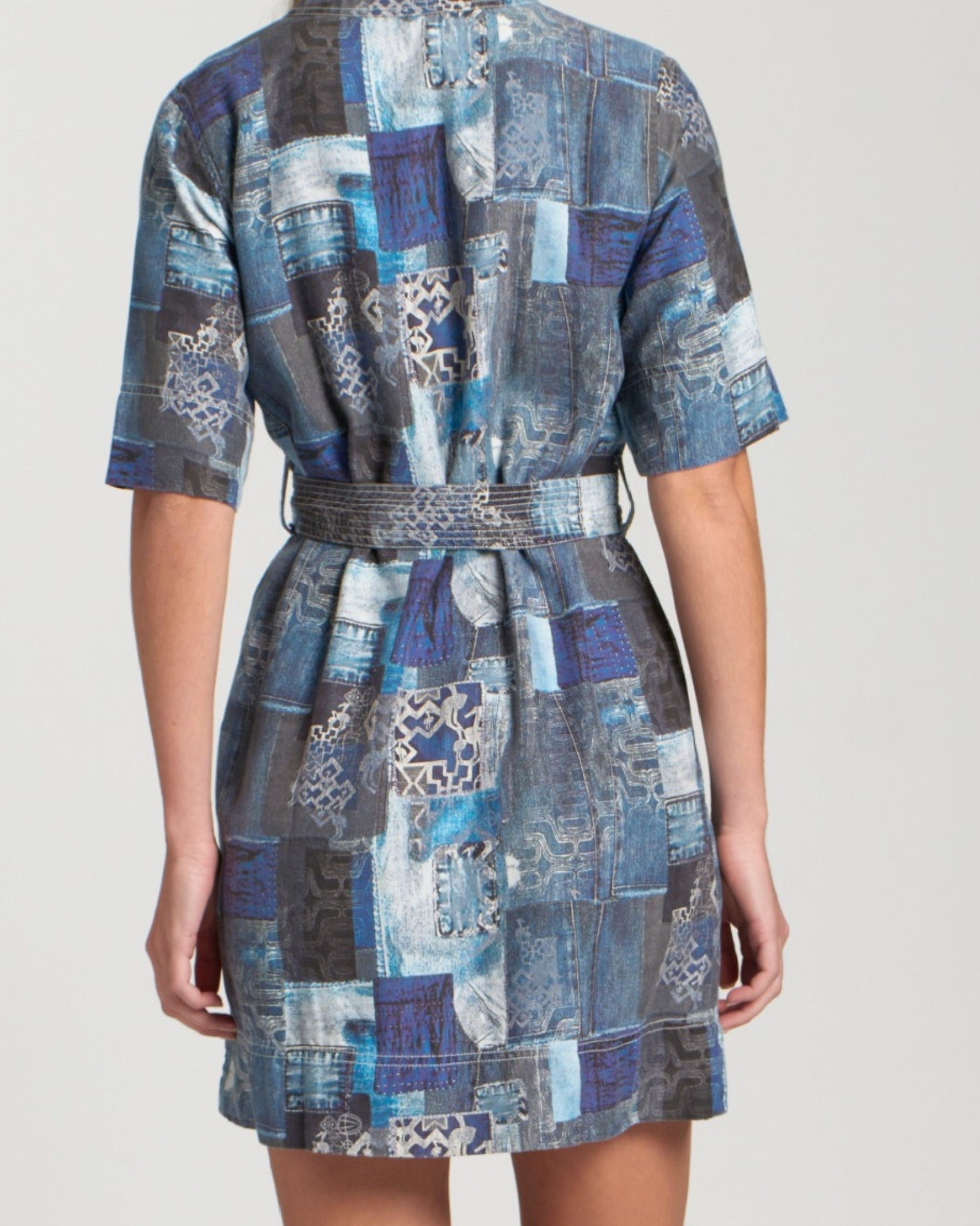 Back view of a person wearing a blue patchwork dress on a plain background