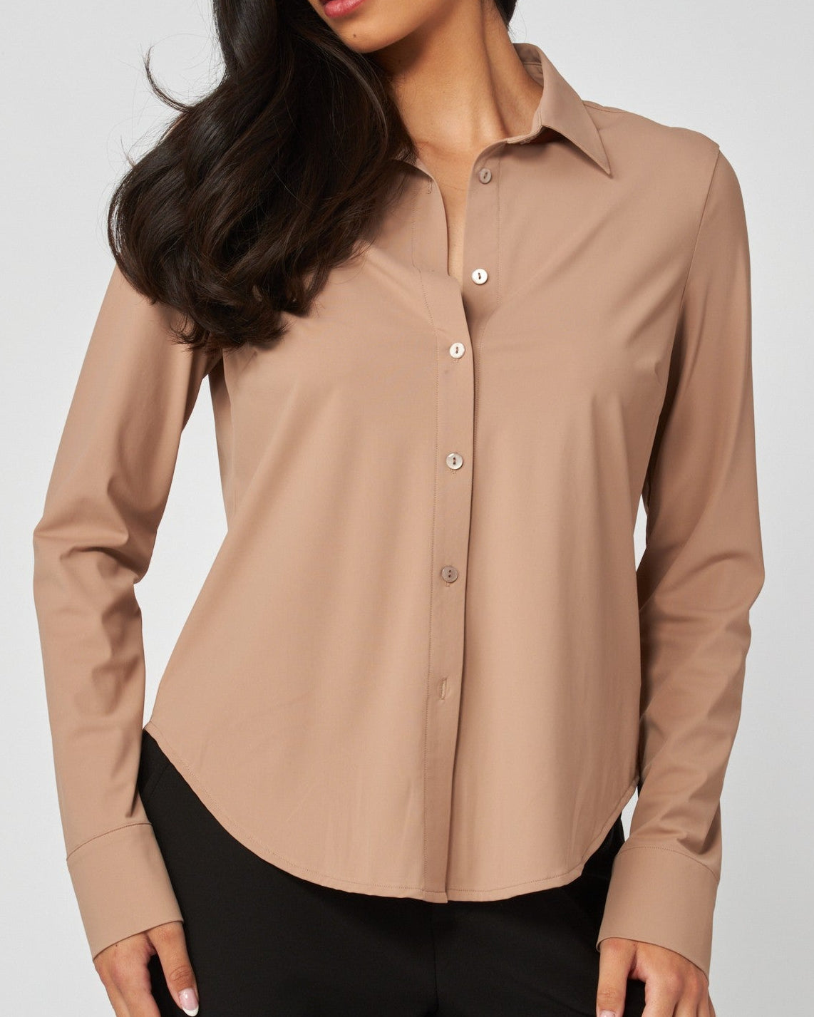 A woman wearing a long-sleeve button-up blouse in a warm taupe-brown color, paired with black pants, photographed against a light gray studio background.