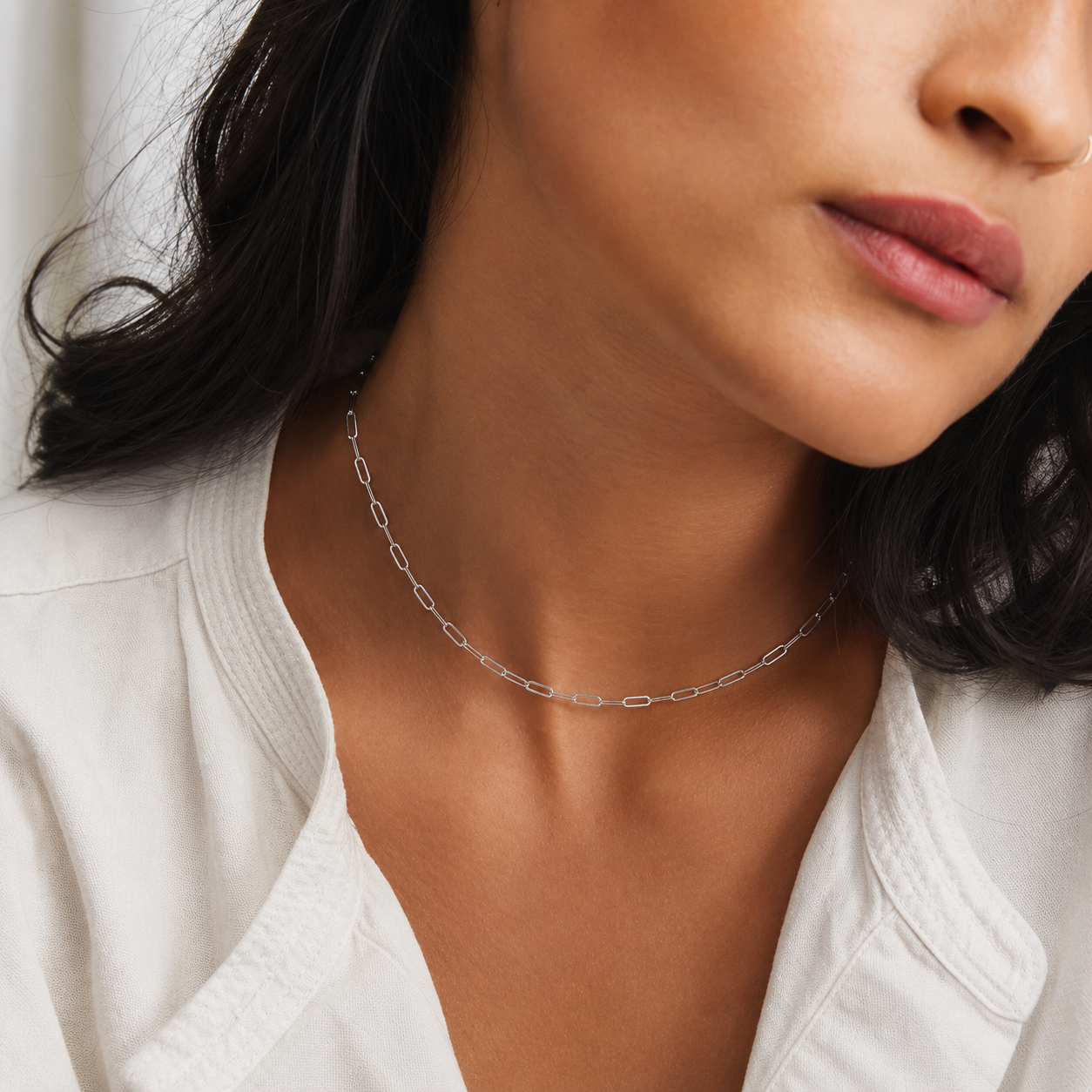 Close-up of a woman wearing a silver necklace with a white top.