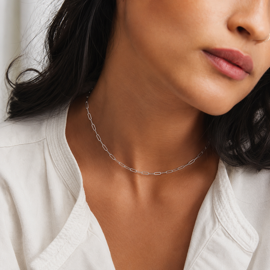 Close-up of a woman wearing a silver necklace with a white top.