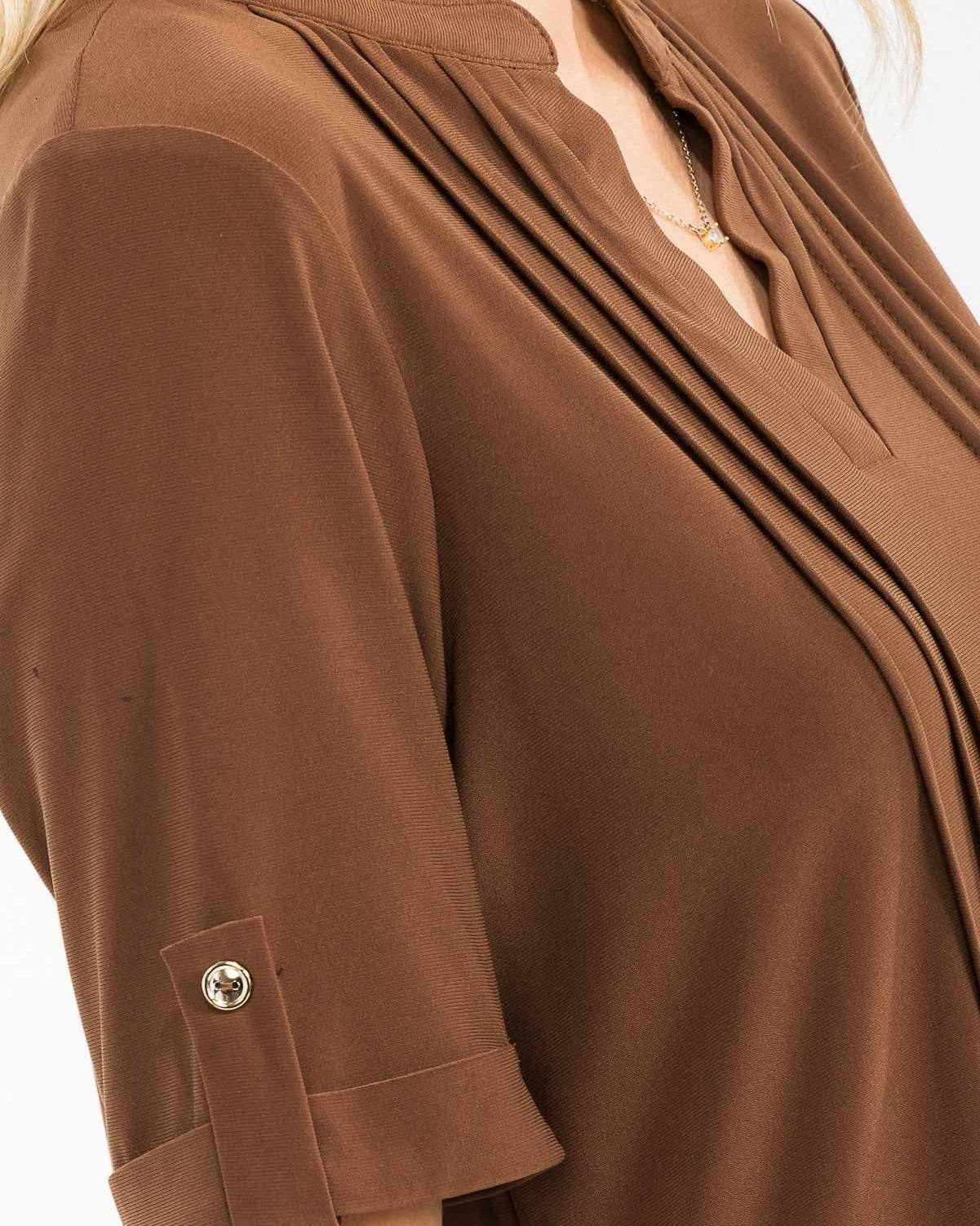 A close-up of a woman wearing a brown short-sleeve blouse with pleated detailing on the chest and a buttoned cuff on the sleeve.