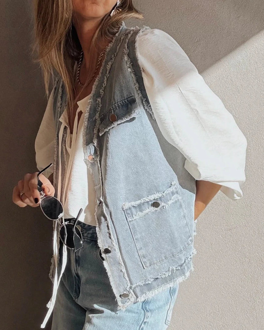 Person wearing a denim vest over a white shirt with a neutral background