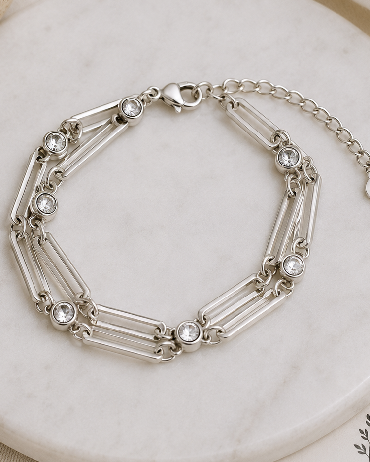 Silver bracelet with gemstones on a marble surface with dried flowers.