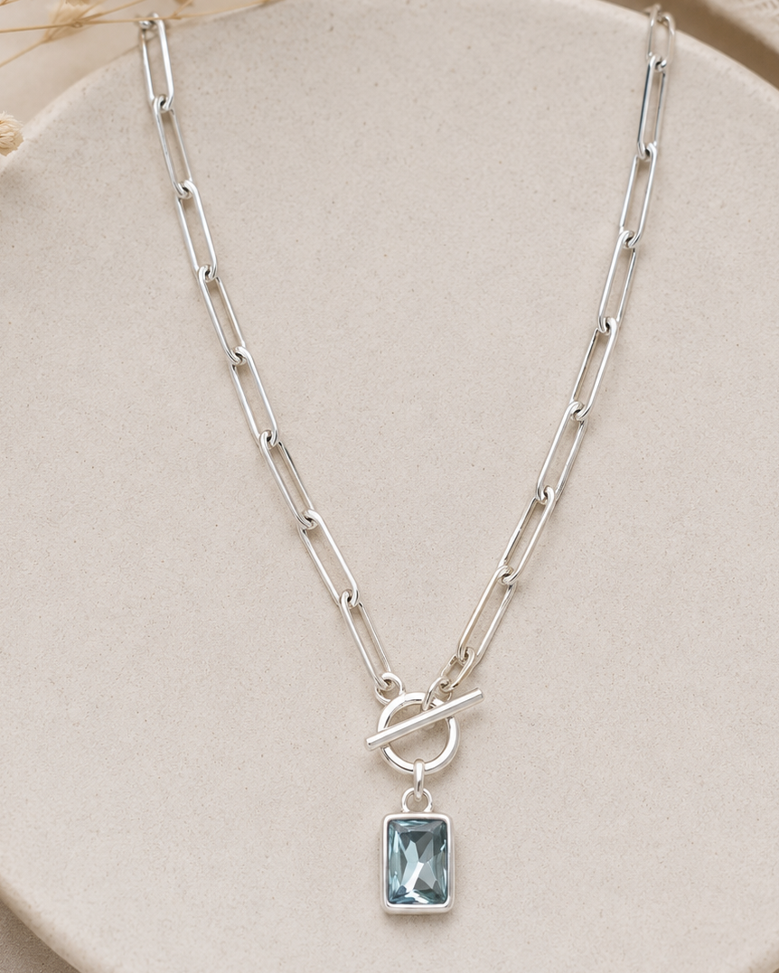 Silver necklace with a blue gemstone pendant on a beige plate.