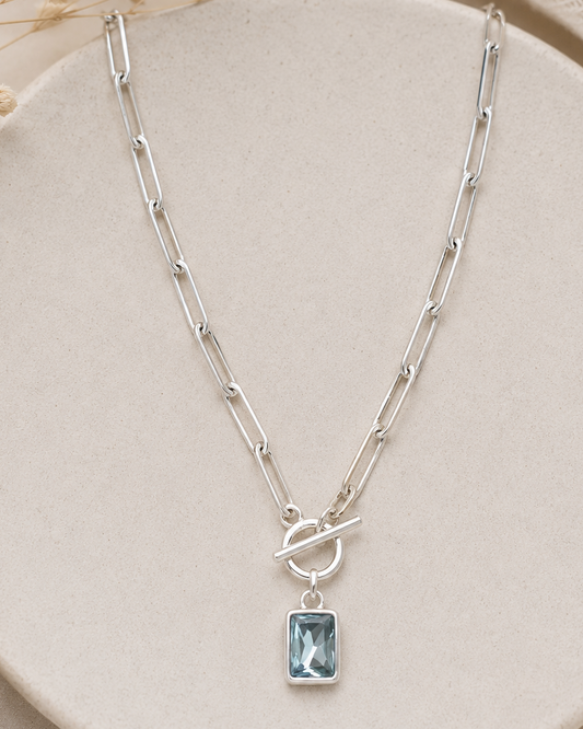 Silver necklace with a blue gemstone pendant on a beige plate.