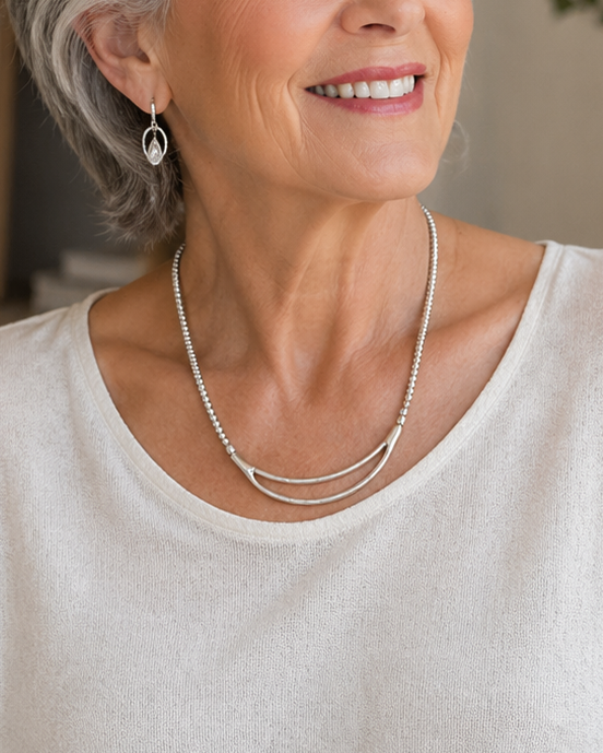 Woman wearing a white top sitting in a cozy room with a plant and framed picture in the background.