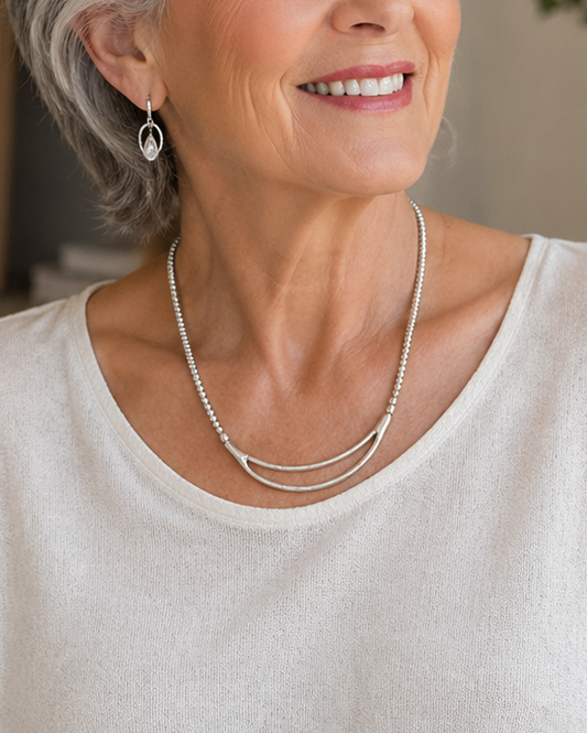 Woman wearing a white top sitting in a cozy room with a plant and framed picture in the background.