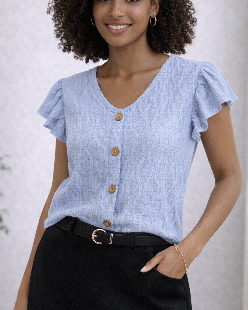 Woman wearing a light blue blouse with ruffled sleeves and black pants against a plain background