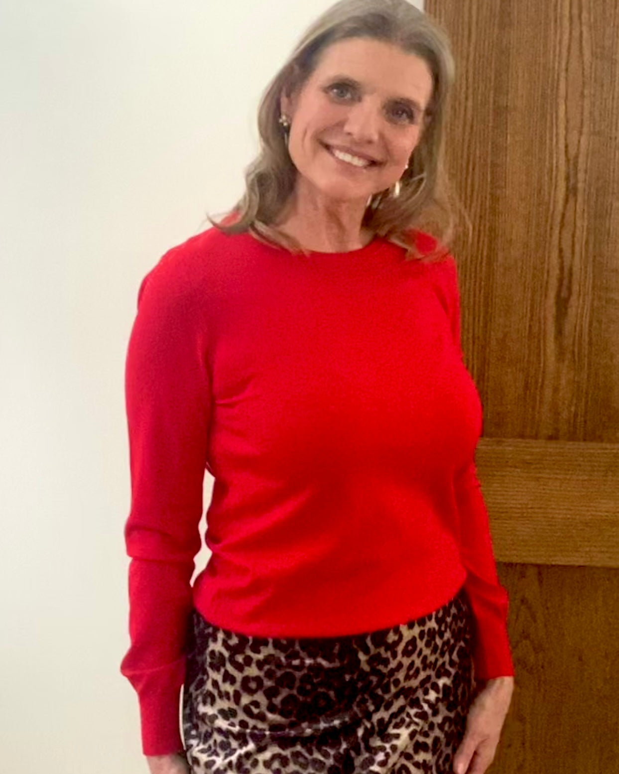 Person wearing a red sweater and leopard print pants standing in front of a wooden door.
