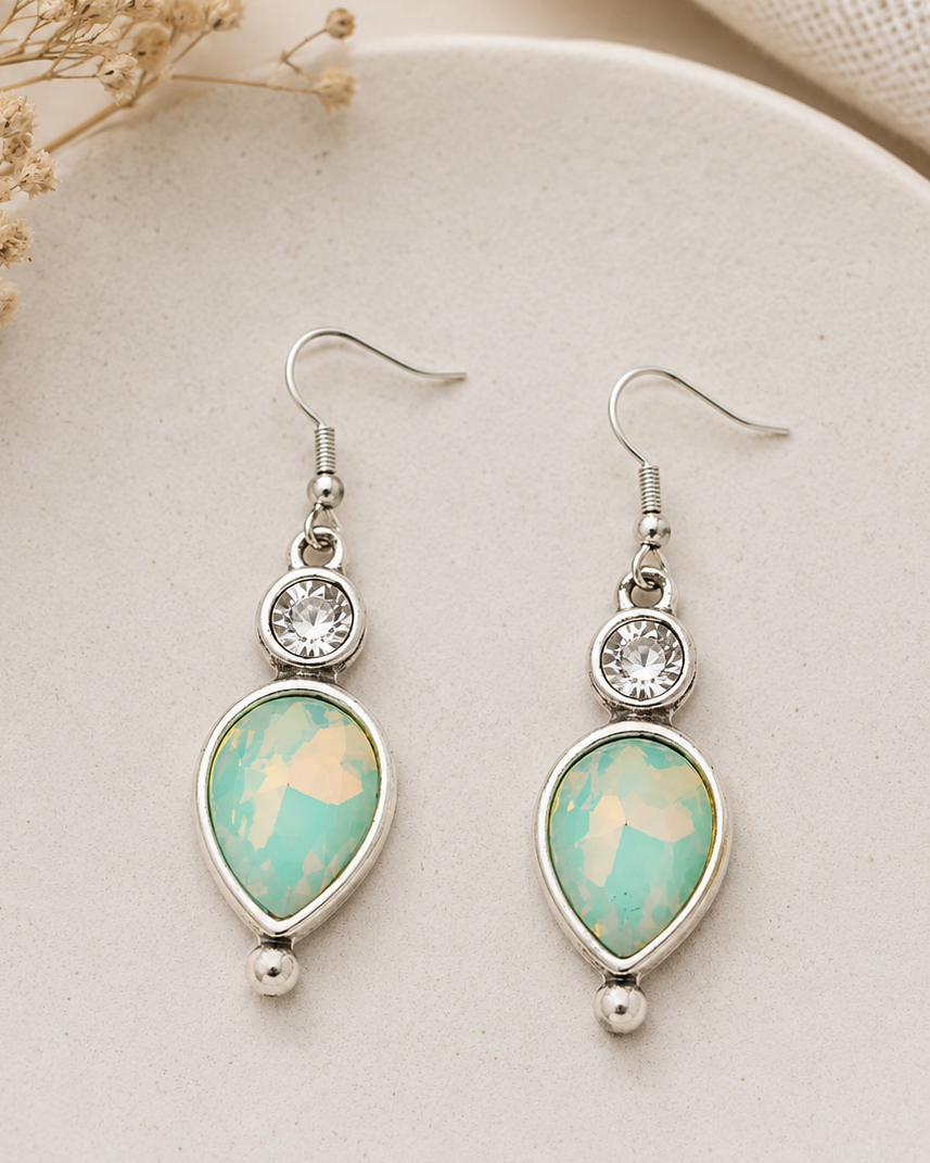 Teardrop-shaped earrings with turquoise stones and silver accents on a beige plate.
