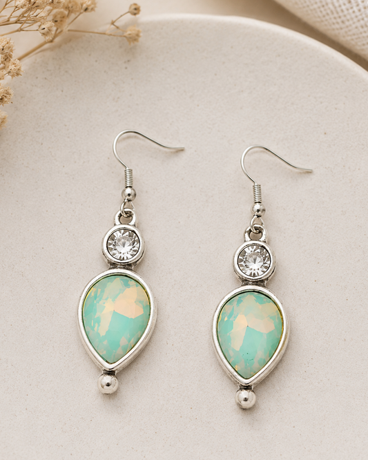 Teardrop-shaped earrings with turquoise stones and silver accents on a beige plate.