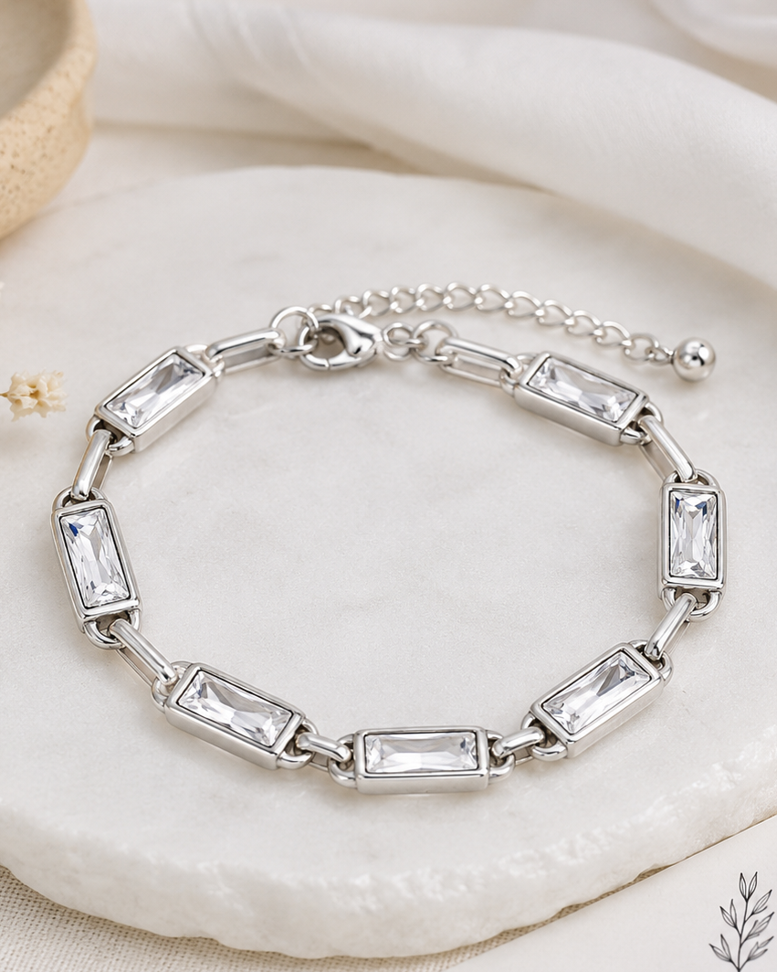 Silver bracelet with clear stones on a white stone surface with dried flowers and a card.
