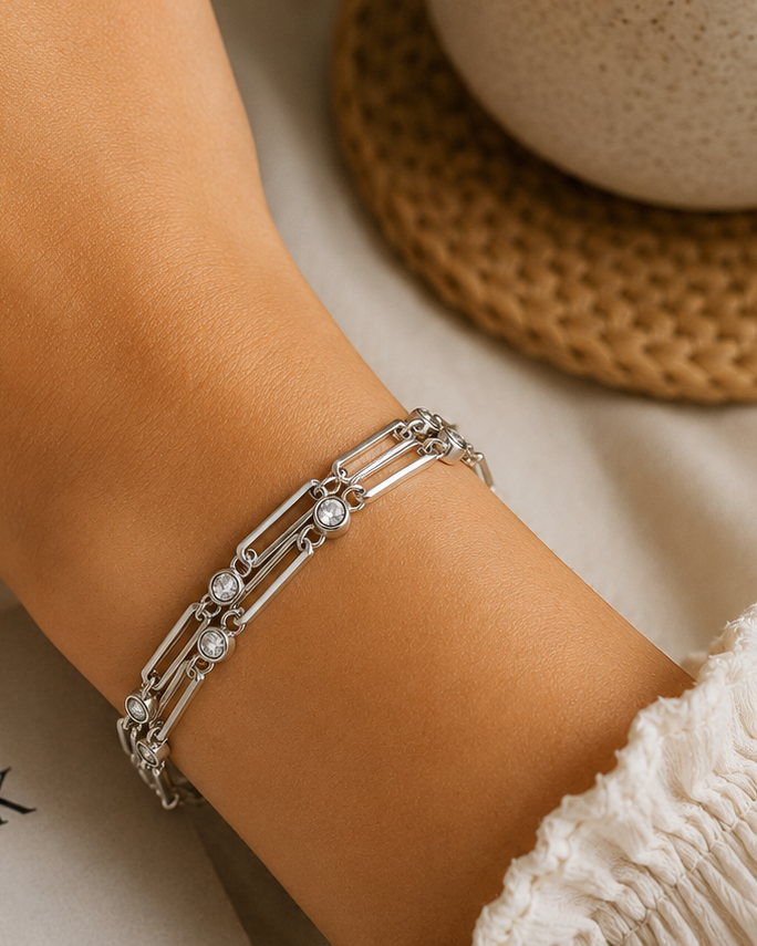 Hand wearing a silver bracelet on a table with a cup and book