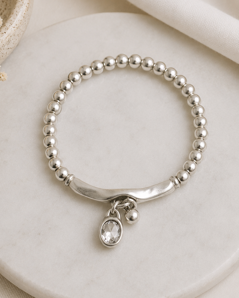 Silver beaded bracelet with a charm on a marble surface, with 'Her Happy Place' branding.