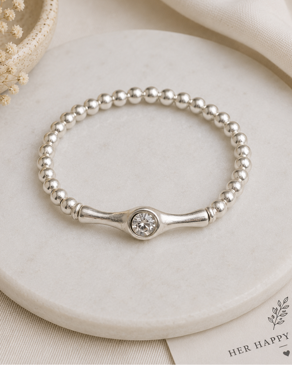 Silver beaded bracelet with a central gemstone on a marble surface with dried flowers.