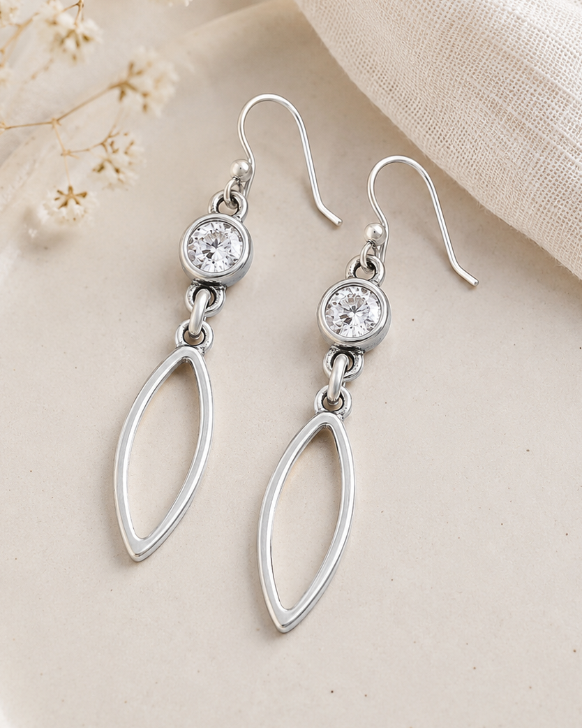 Silver earrings with clear stones on a beige plate with delicate flowers