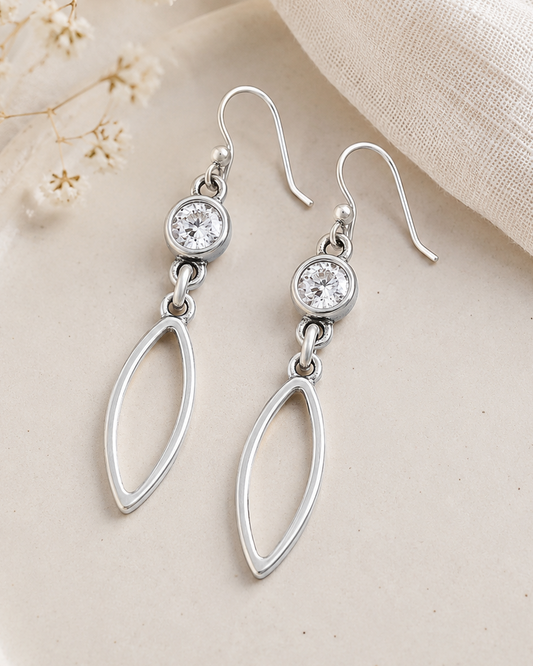 Silver earrings with clear stones on a beige plate with delicate flowers