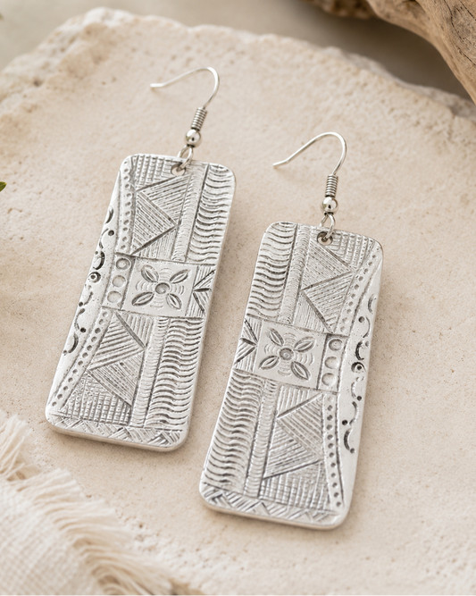 Silver patterned earrings on a textured stone surface with natural elements.