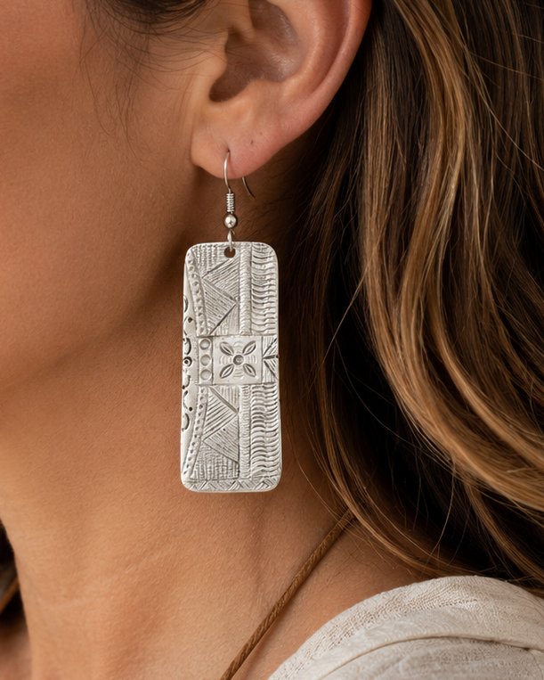 Woman wearing a silver earring with a decorative pattern, indoors.