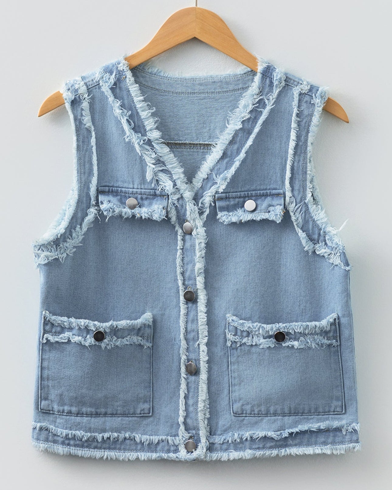 Light blue denim vest on a wooden hanger against a white background