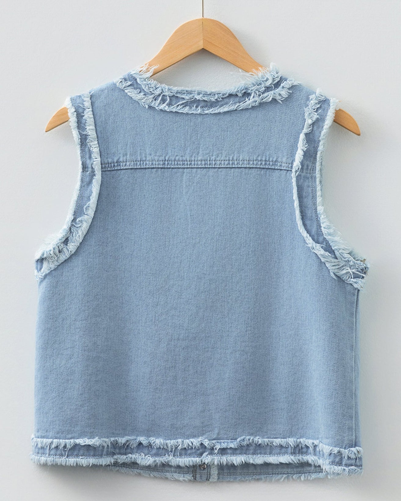 Light blue denim vest on a wooden hanger against a white background