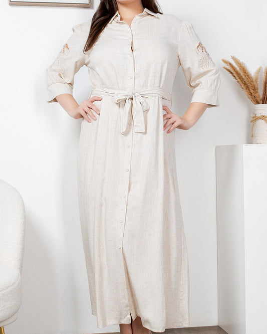 Woman wearing a long beige dress in a minimalistic room.